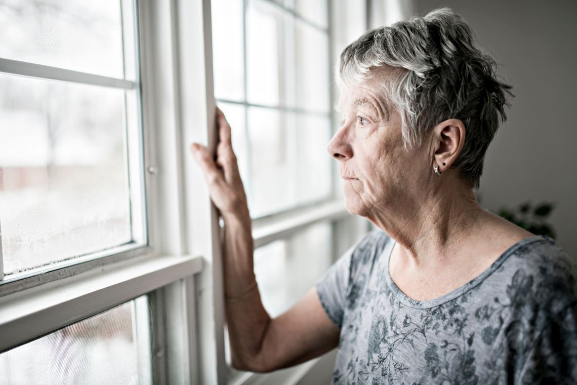 Angst vor dem Alleinsein: ältere Dame schaut gedankenverloren aus dem Fenster