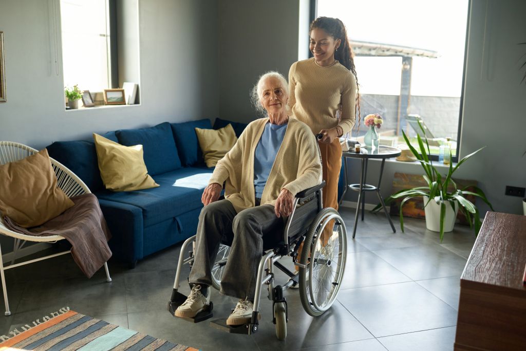 Eine junge Haushaltshilfe kümmert sich um eine ältere Dame im Rollstuhl