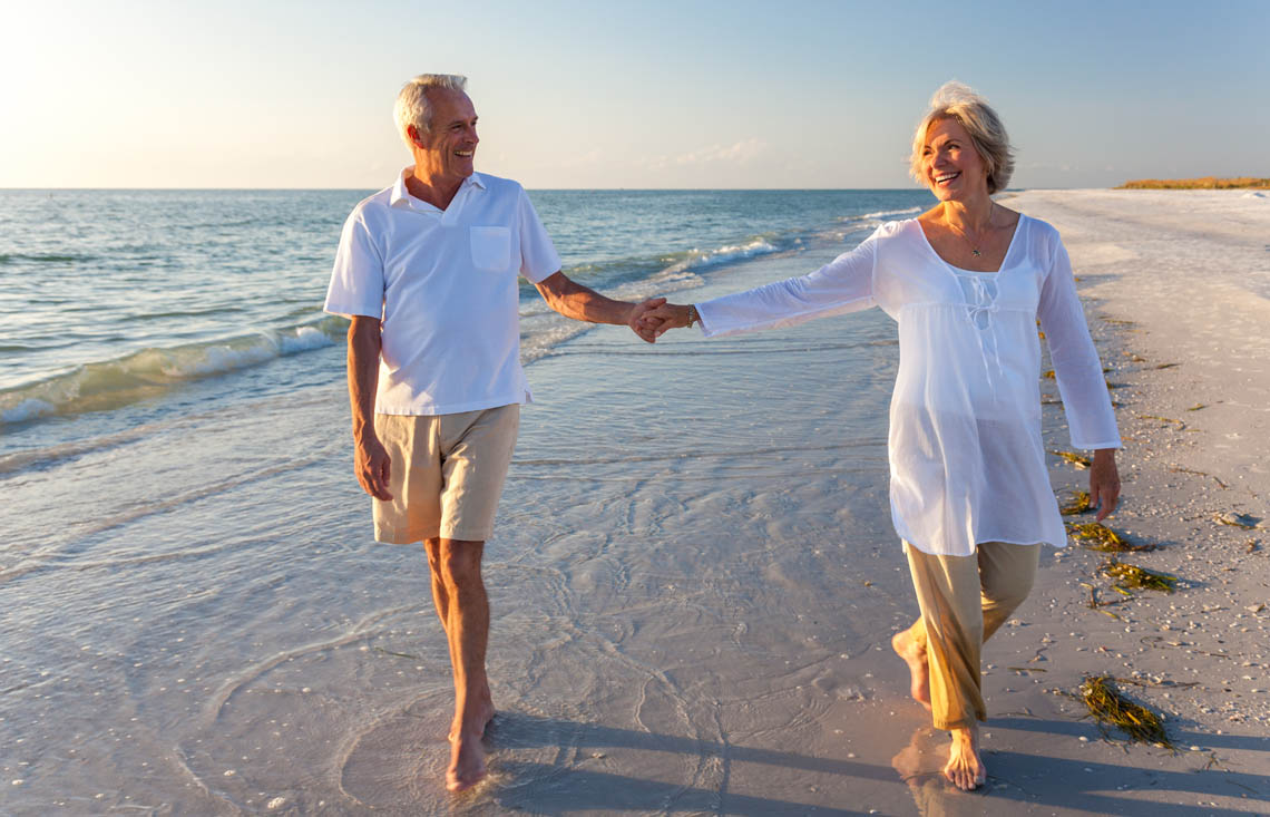 Älteres Paar spaziert Hand in Hand am Strand