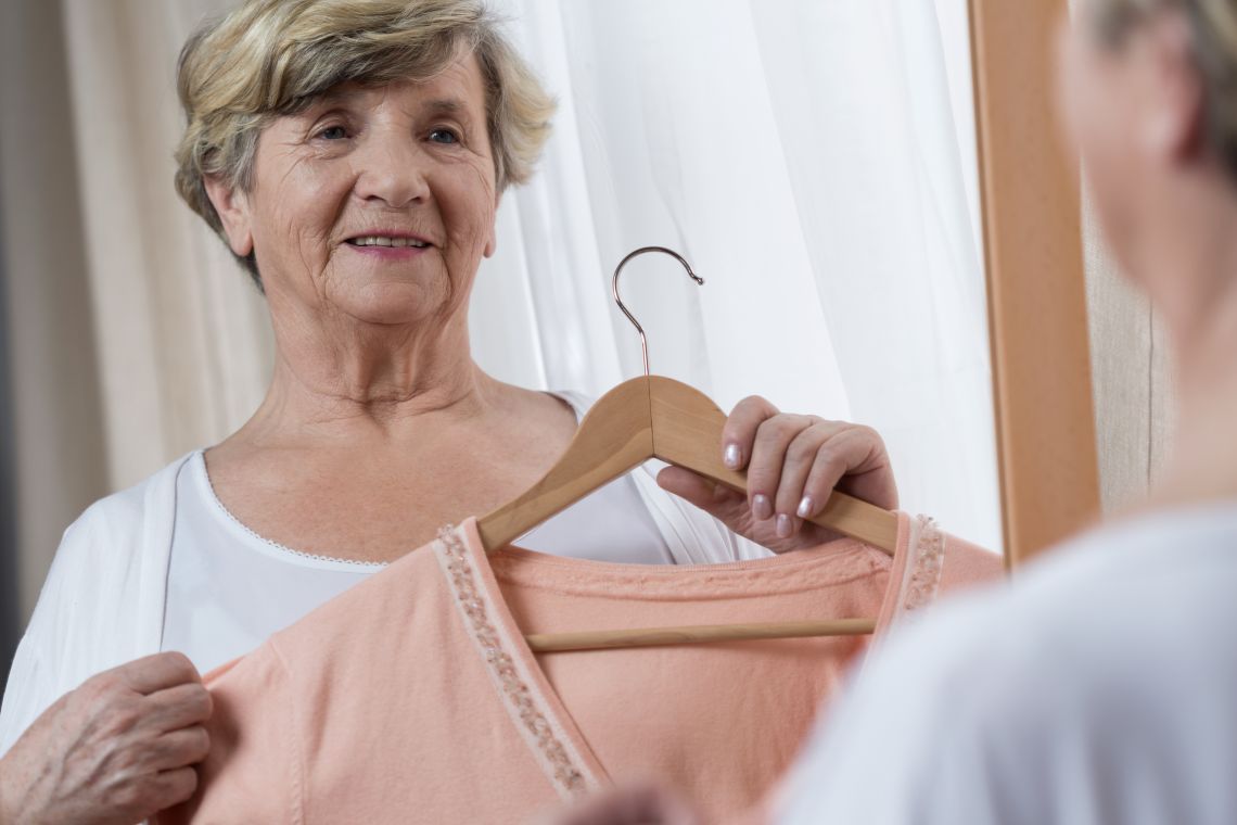 Seniorengerechte Kleidung: Frau hält Oberteil auf Bügel fest