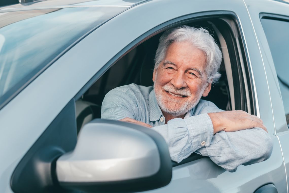 Ein Rentner sitzt glücklich in seinem Auto auf dem Fahrersitz