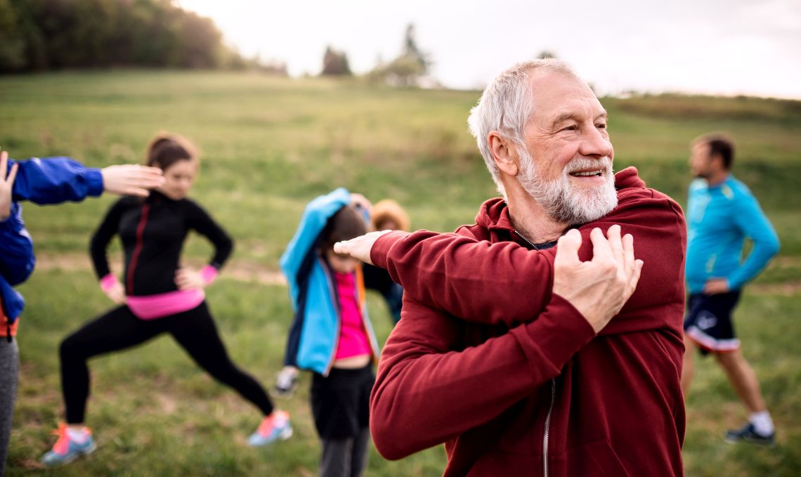 Ein Senior macht mit einer Gruppe Menschen Sportübungen im Freien