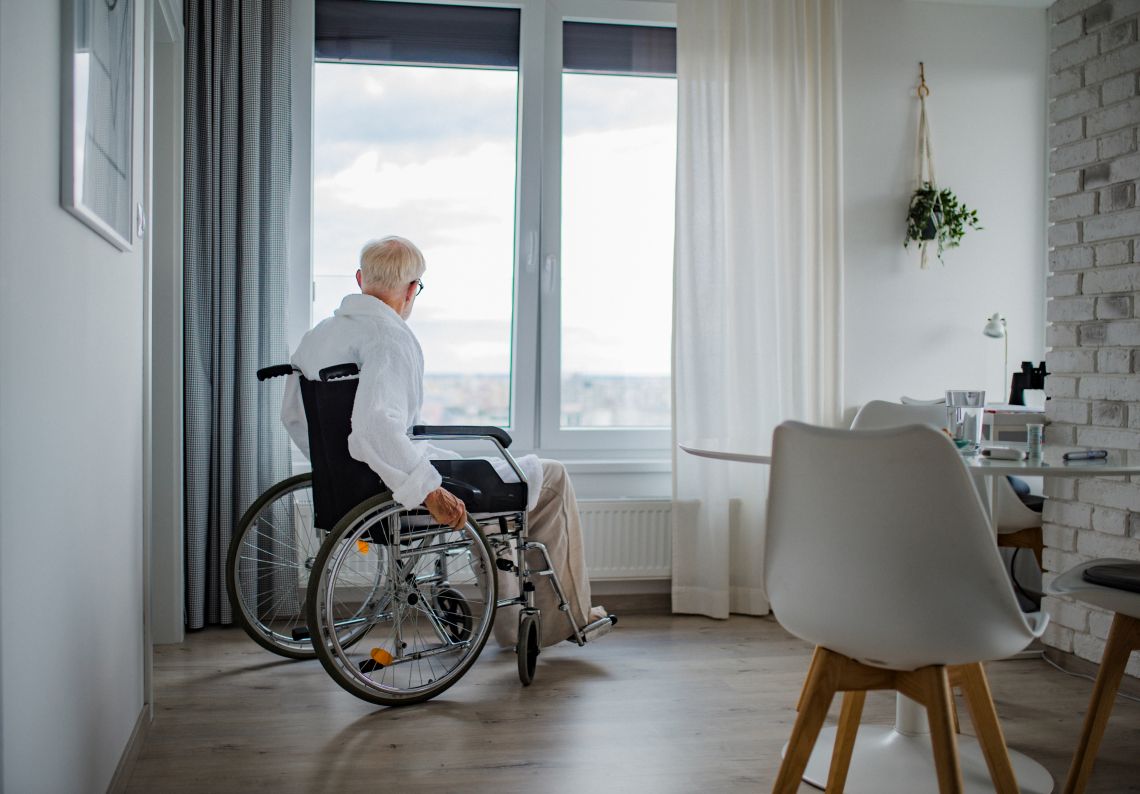 Angst vor dem Alleinsein: Ein Senior in einem Rollstuhl ist allein zuhause und schaut aus dem Fenster