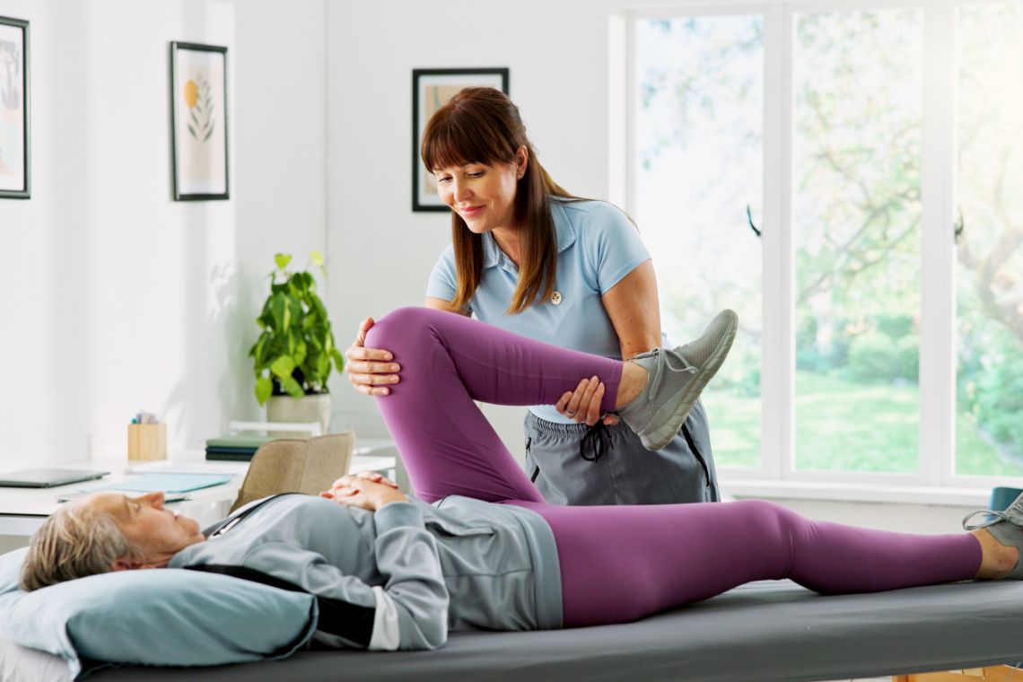 Eine Physiotherapeutin führt bei einer Frau Beinübungen durch