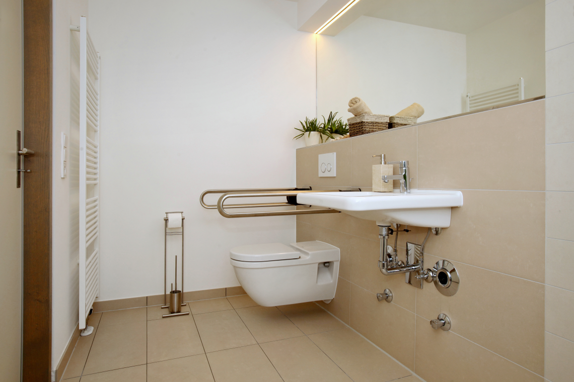 Barrierefreies Badezimmer mit unterfahrbarem Waschbecken, WC und Haltegriffen.