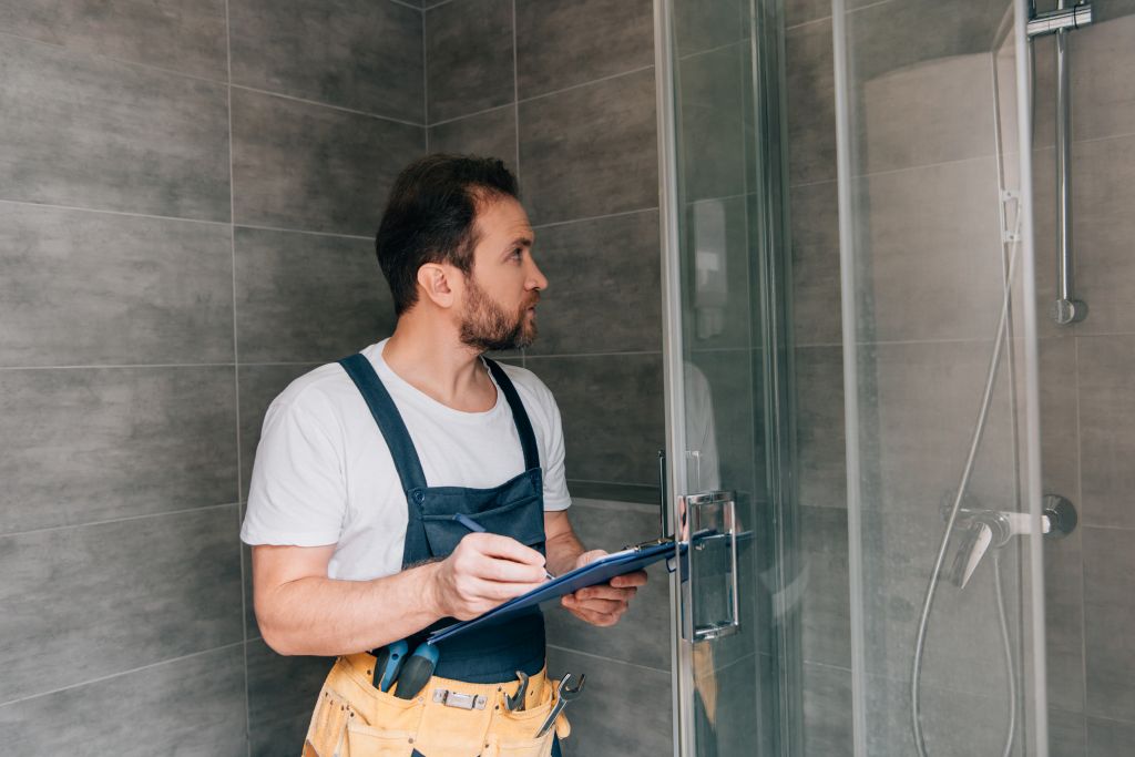 Professionelle Unternehmen kümmern sich um die fachgerechte Umsetzung von barrierefreien Maßnahmen im Bad © © LIGHTFIELD STUDIOS | stock.adobe.com Barrierefreies Bad: Ein Handwerker mit Klemmbrett überprüft die Dusche in einem Badezimmer