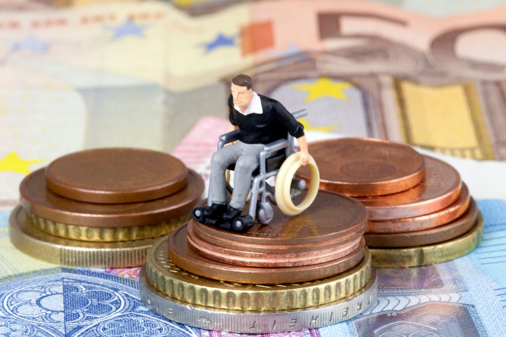 Eine kleine Modellfigur eines Rollstuhlfahrers steht auf Münzen
