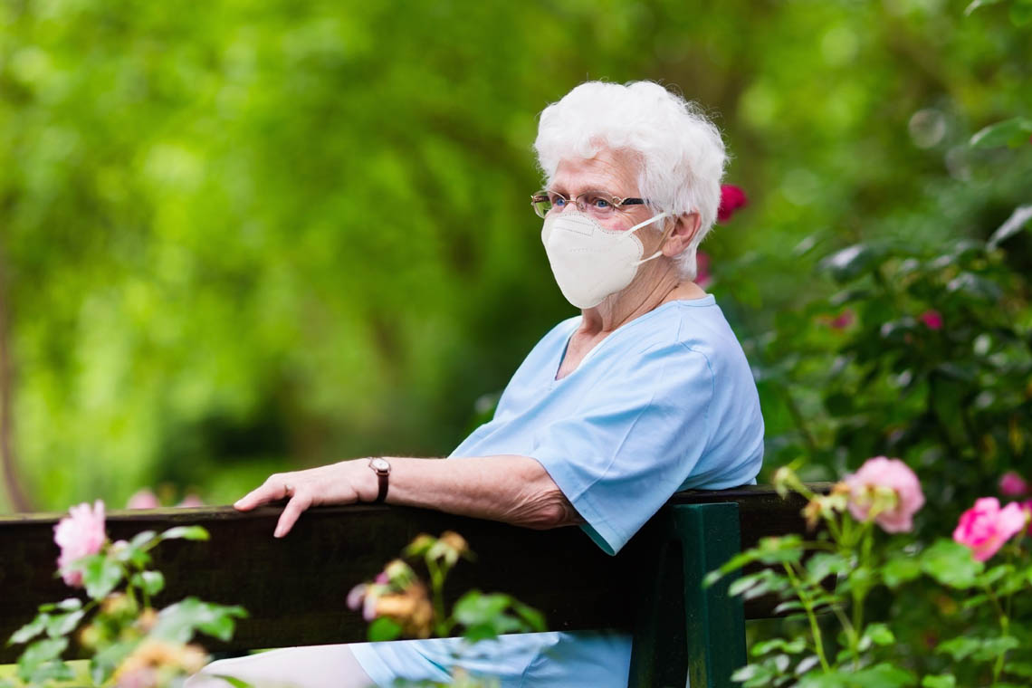 Seniorin mit FFP2-Maske sitzt auf Parkbank