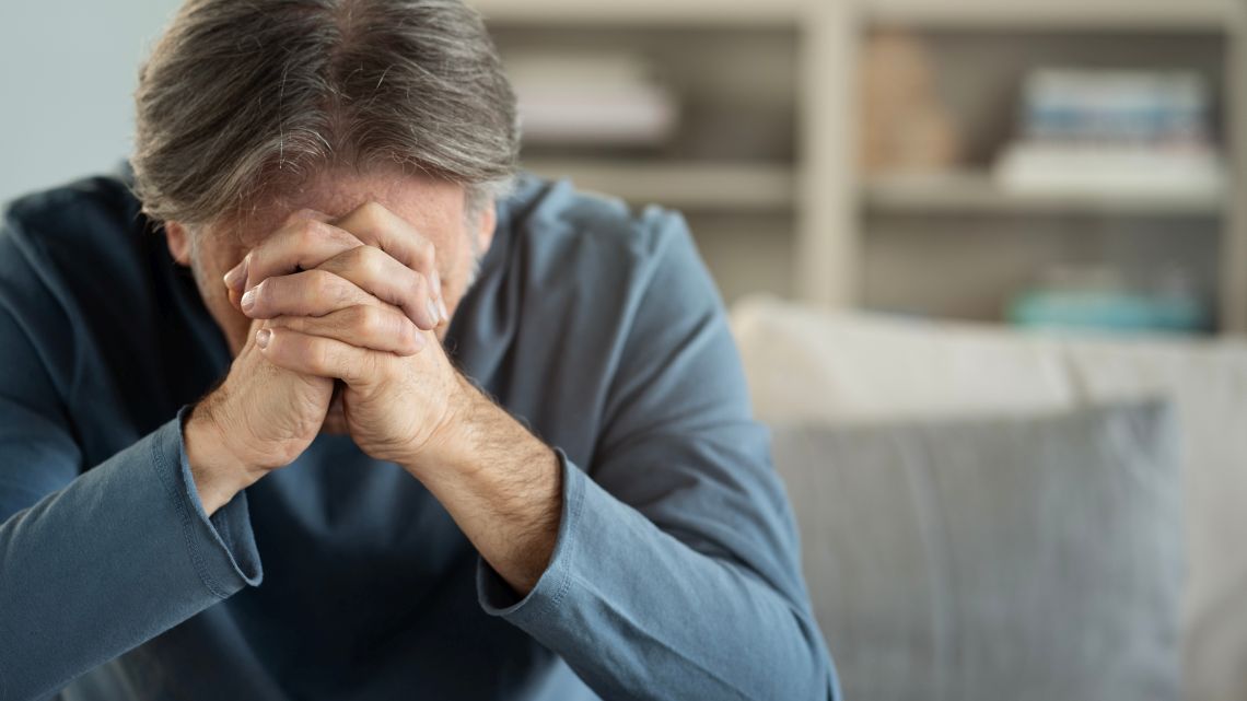 Einsamkeit nach Tod des Partners: Ein älterer Mann stützt seinen Kopf traurig auf seinen gefalteten Hände ab