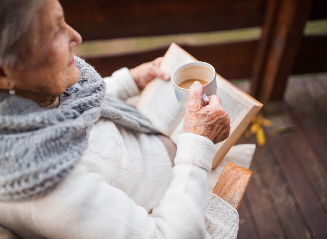 Seniorin liest draußen ein Buch und trinkt Kaffee