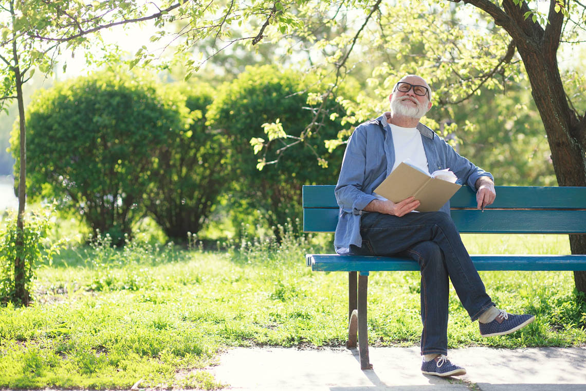 Älterer Mann sitzt auf einer Bank und lernt eine Sprache