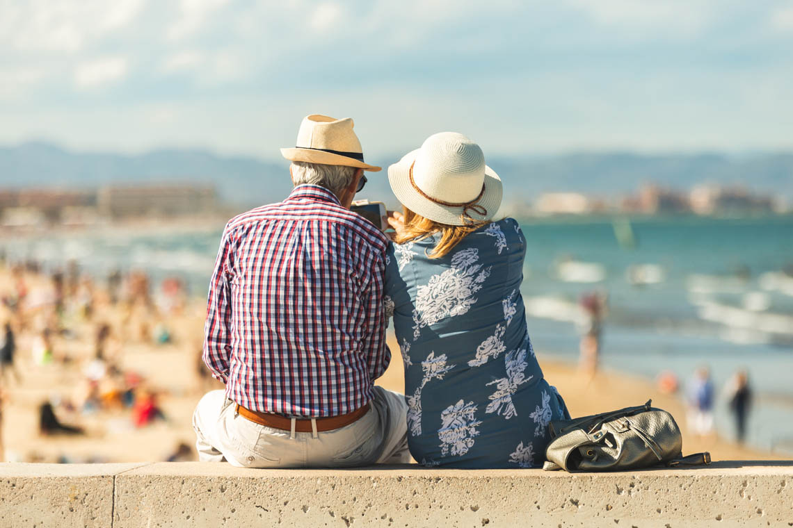 Älteres Paar sitzt an Strand und macht ein Foto