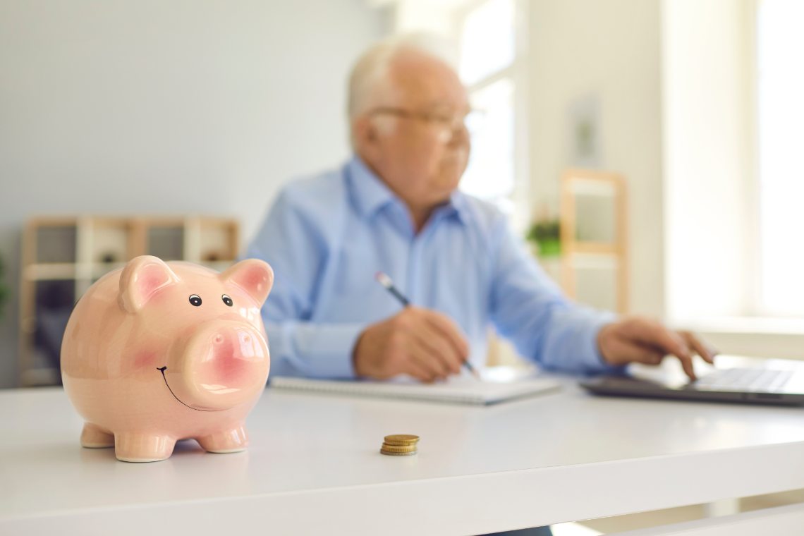 Rosa Sparschwein, Renter am Laptop im Hintergrund