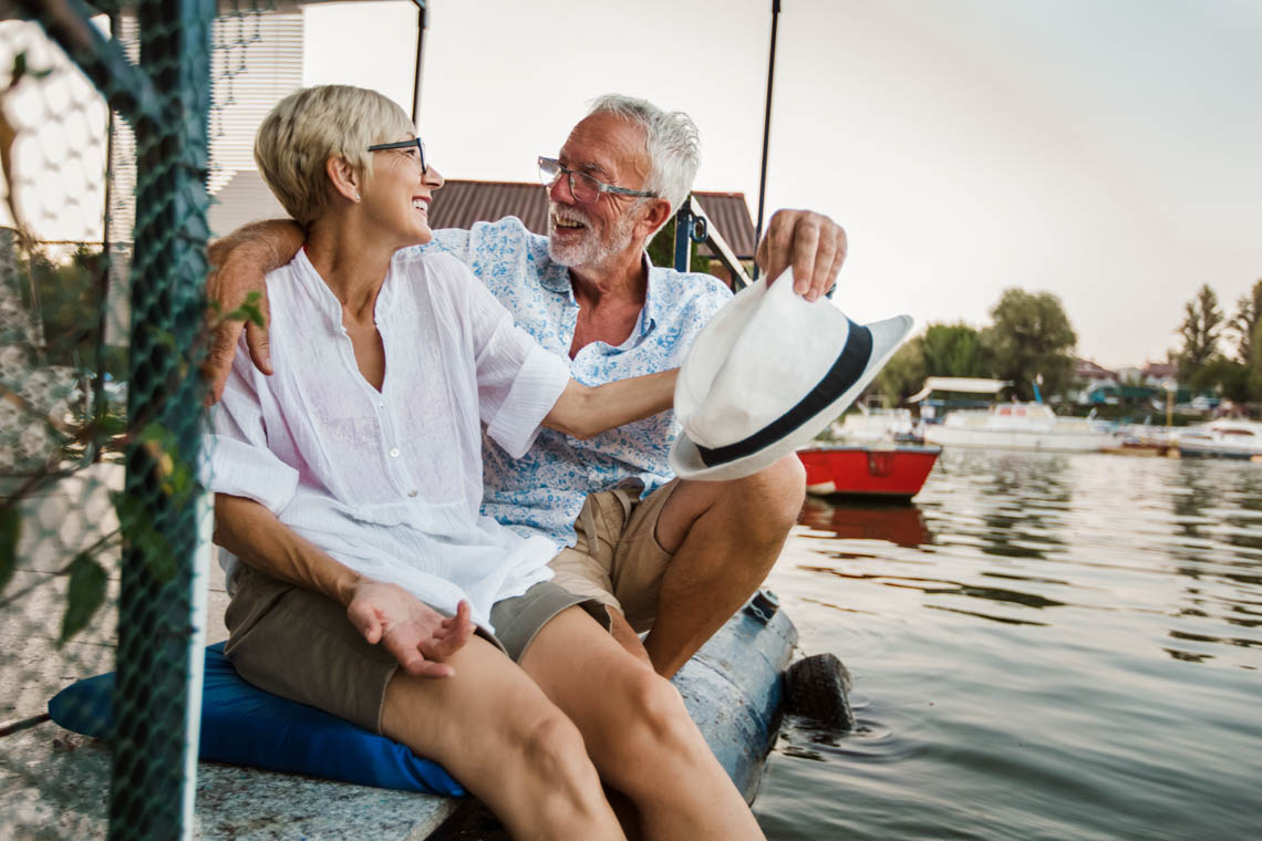 Älteres Paar sitzt am Wasser und lächelt sich an