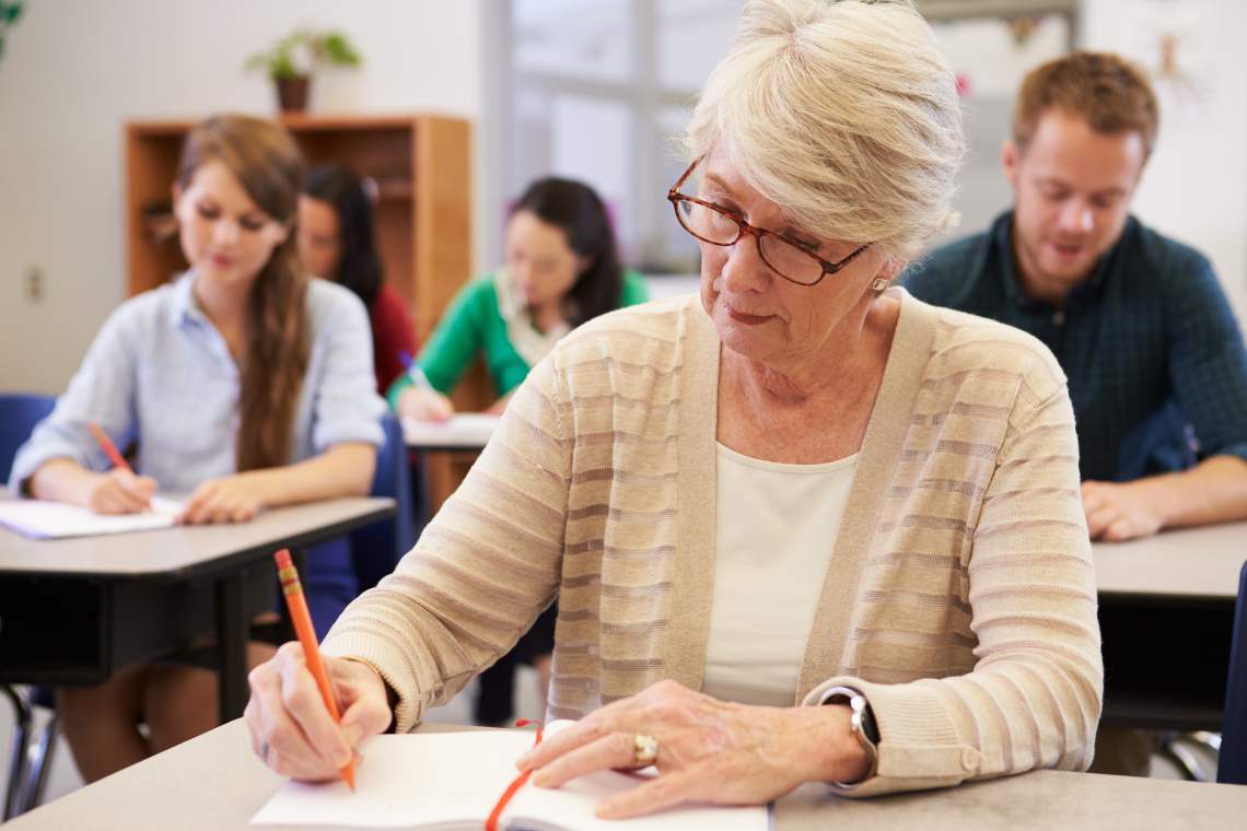 Seniorin sitzt in einem Klassenzimmer und schreibt in ein Buch