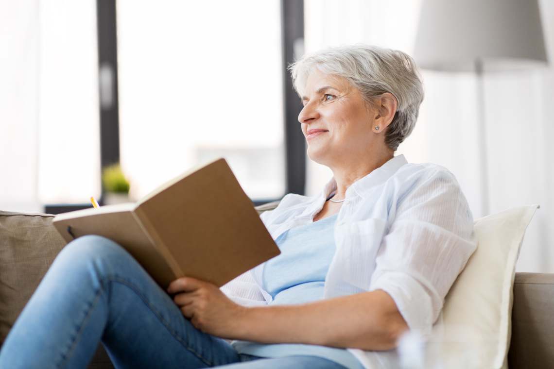 Frau sitzt mit einem Notizbuch auf dem Sofa und schaut in die Luft