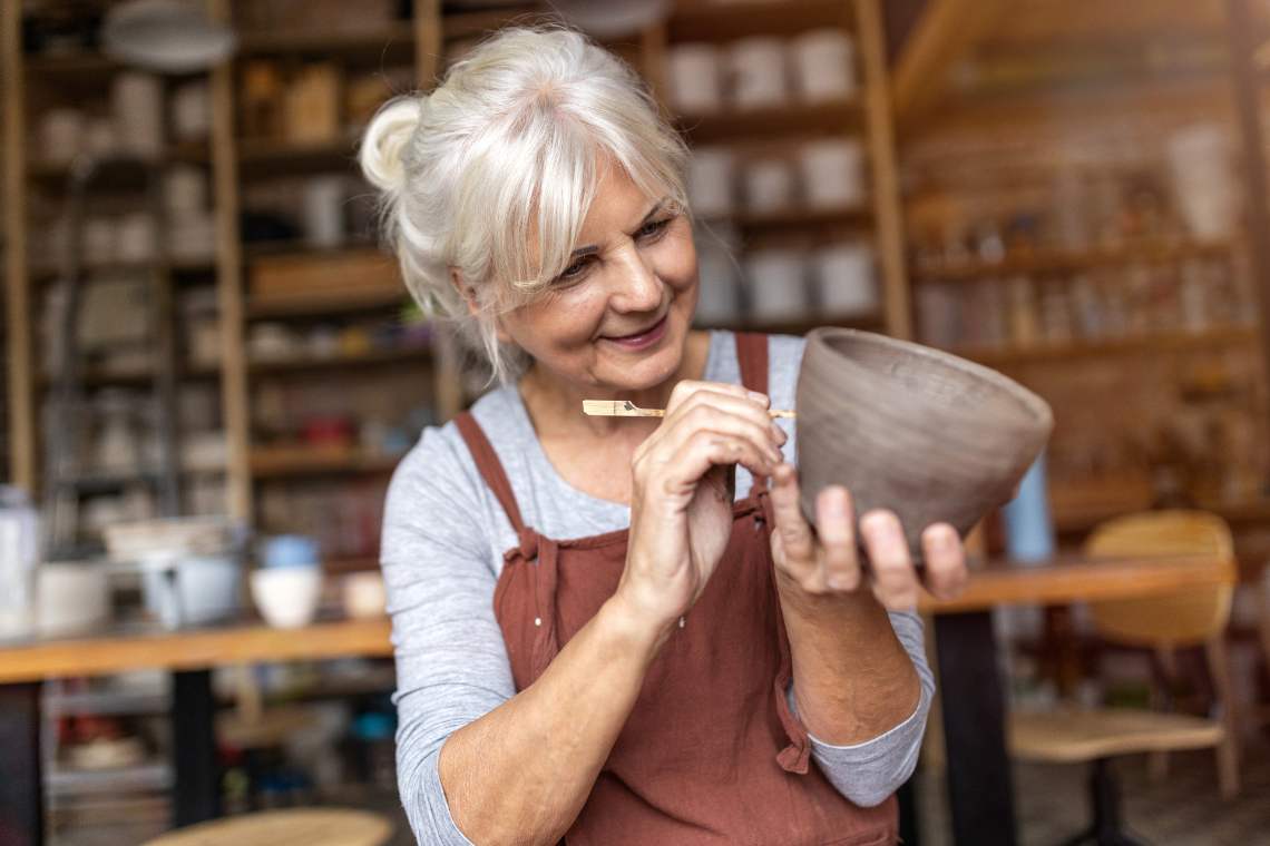 ältere Frau verziert einen selbstgemachten Keramiktopf
