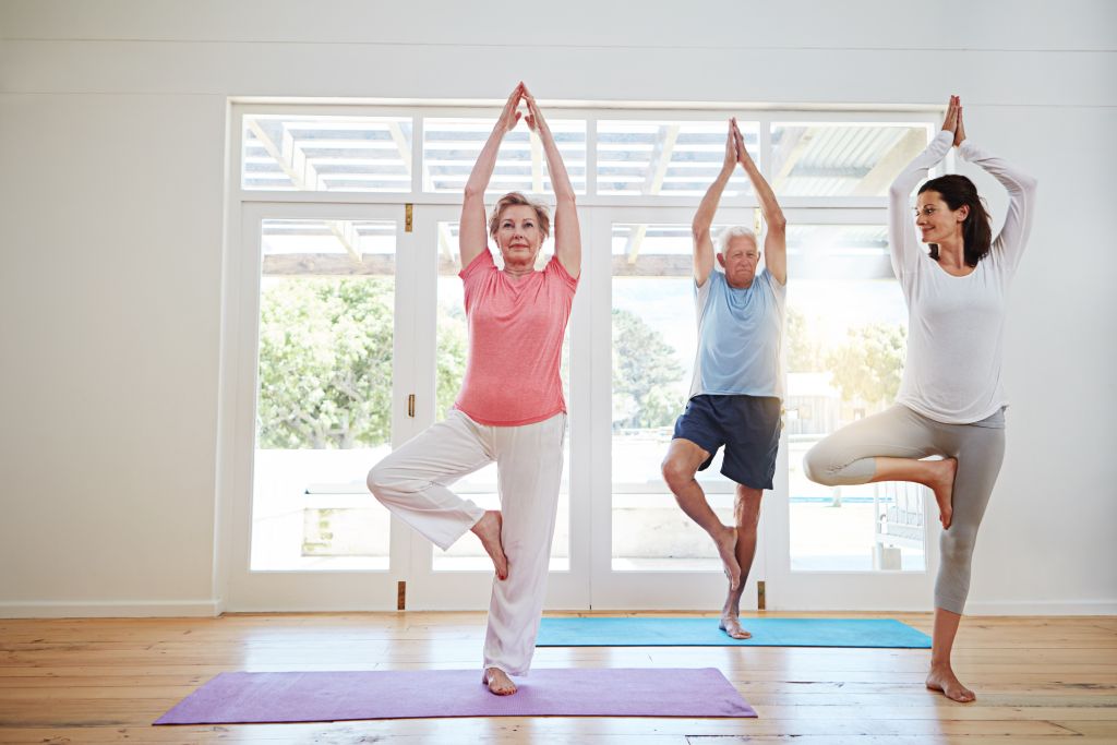 Zwei ältere Personen führen zusammen mit einer Yogalehrerin eine Übung durch