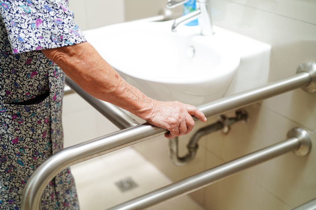 Nahaufnahme einer älteren Frau, die sich an Haltegriffen neben einem Waschbecken festhält
