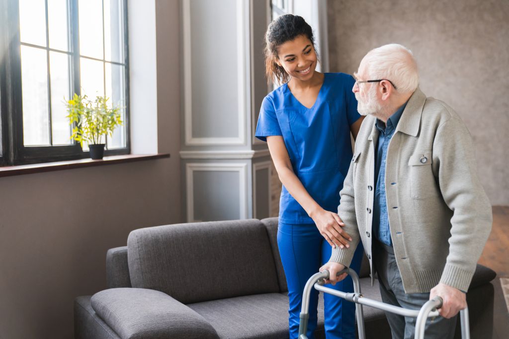 Eine junge Krankenpflegerin stützt einen älteren Mann mit Gehhilfe