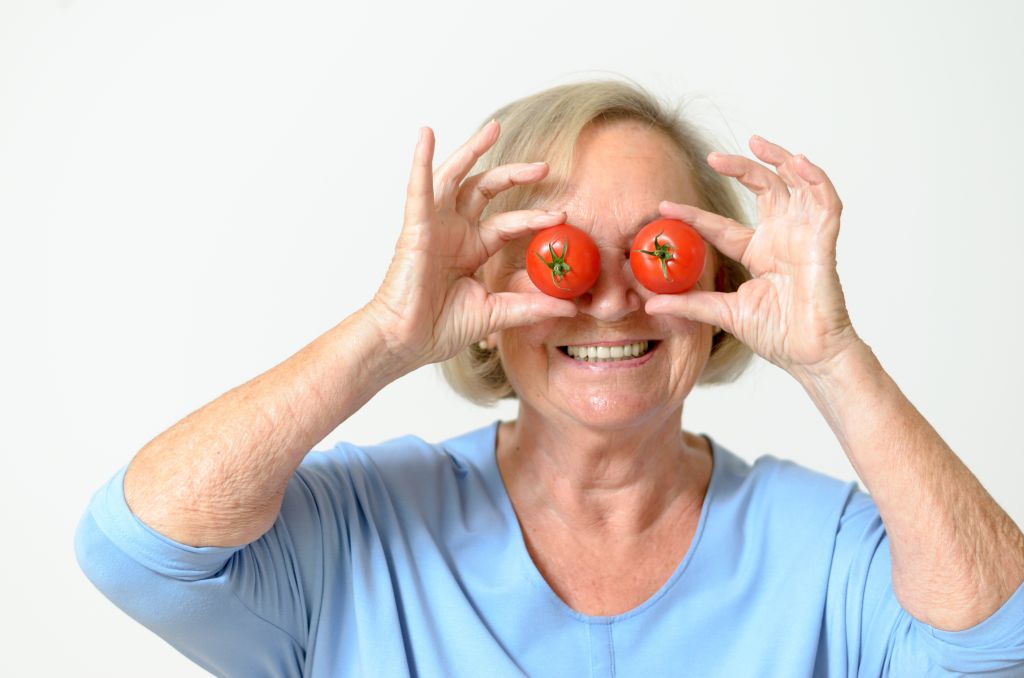 Eine Seniorin hält sich zwei Tomaten vor die Augen