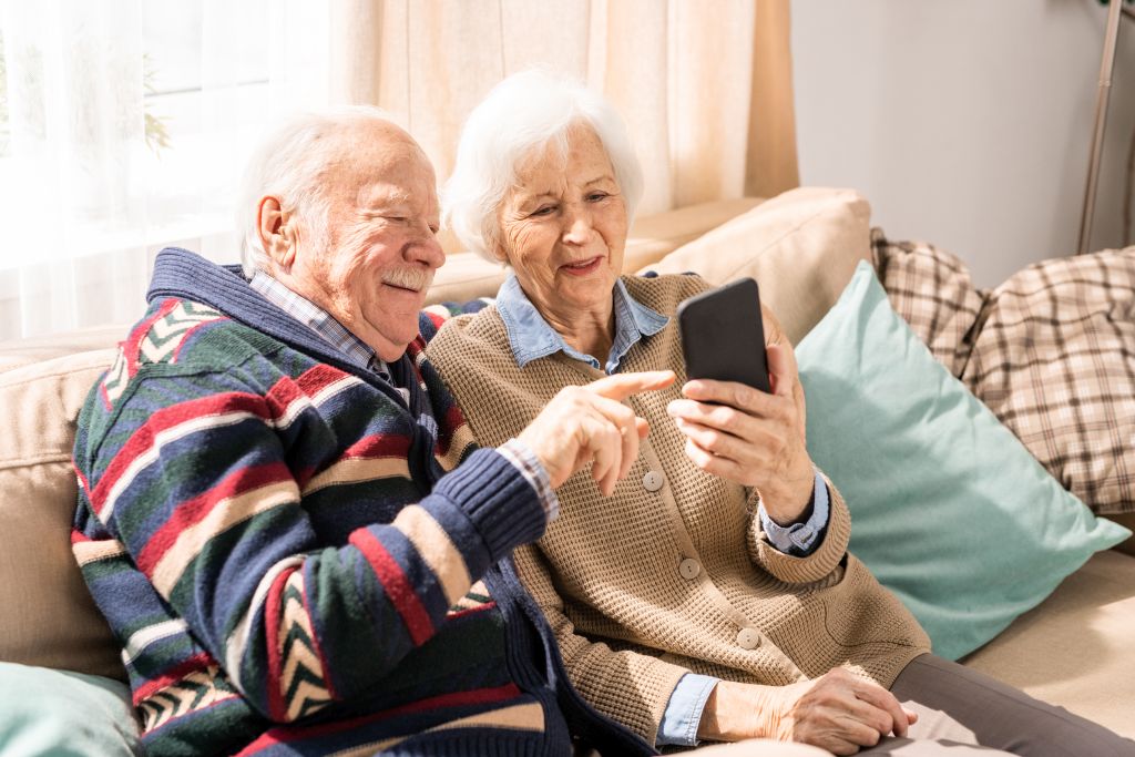 Hilfsangebote für Senioren: Ein älteres Ehepaar schaut gemeinsam vergnügt auf ein Smartphone