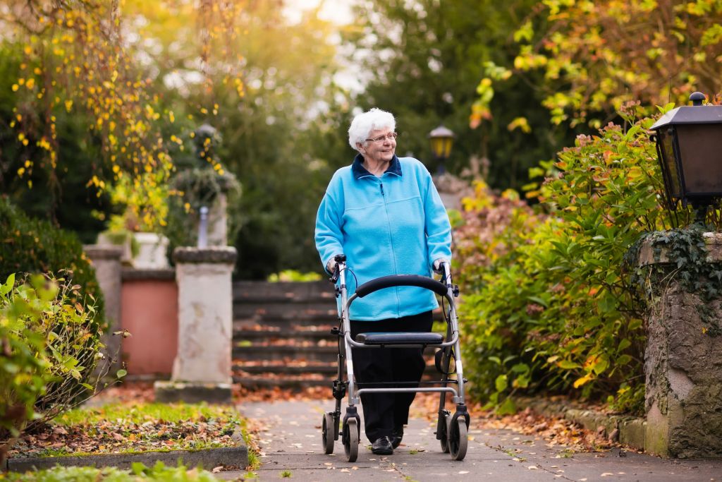 Eine Seniorin mit Rollator beim Spaziergang an der frischen Luft
