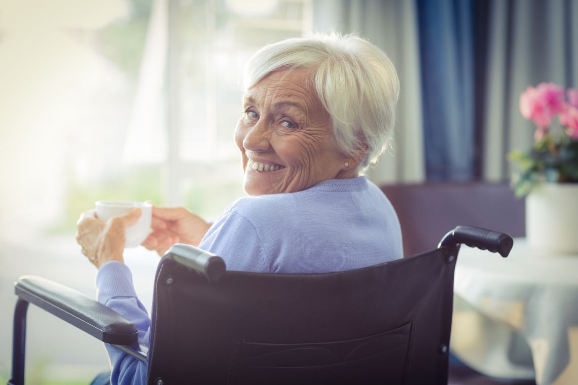 Eine glückliche Seniorin im Rollstuhl blickt lächelnd in die Kamera