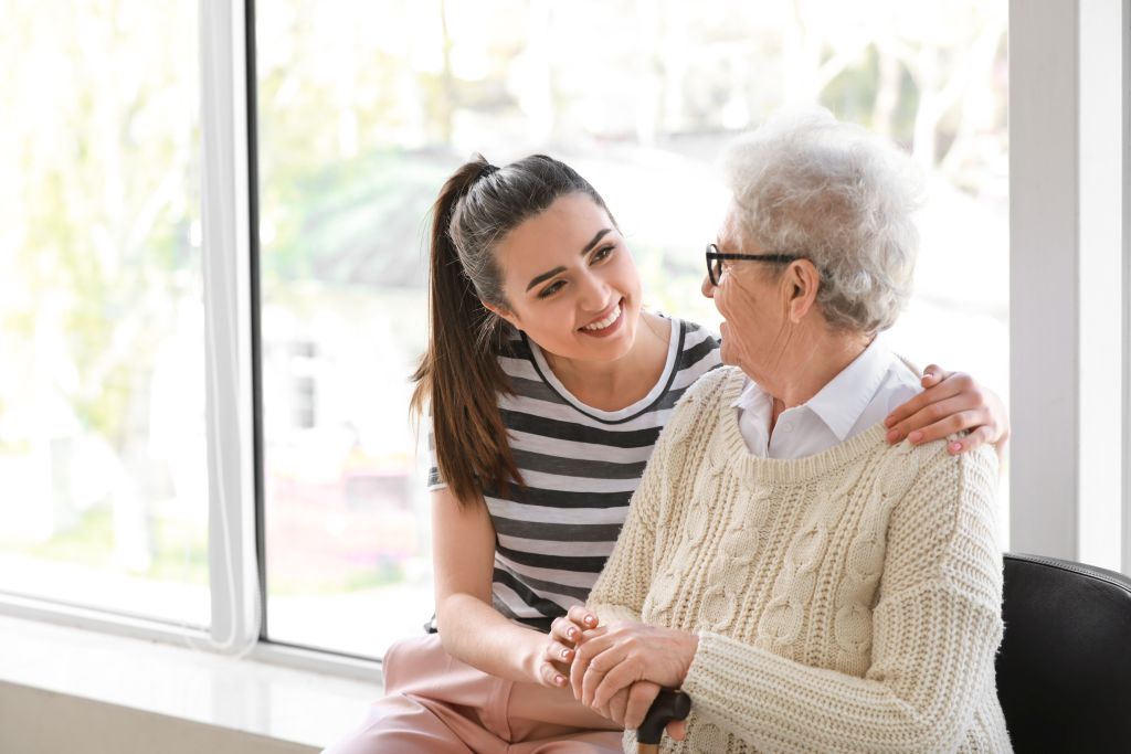 Eine junge Frau umarmt eine Seniorin von der Seite und lächelt sie an
