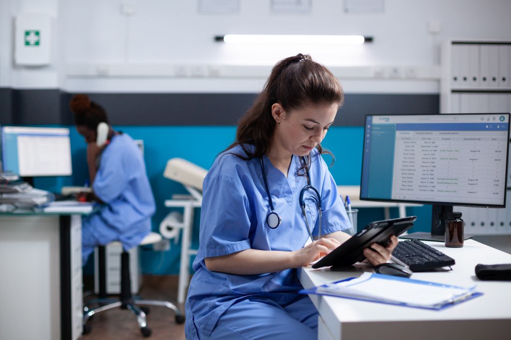 Eine junge Ärztin sitzt in einem Krankenhaus-Büro und schaut sich etwas auf einem Tablet an