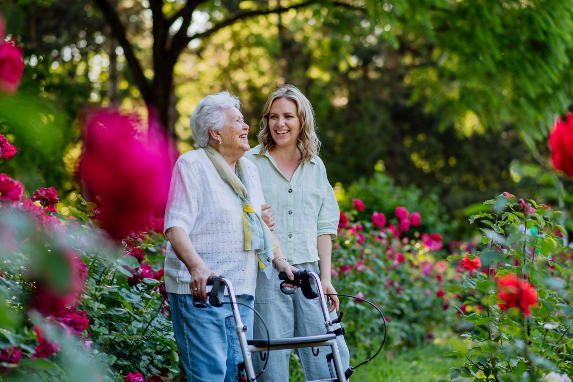 Körperliche Veränderungen im Alter: Seniorin mit Rollator geht mit Begleitung spazieren