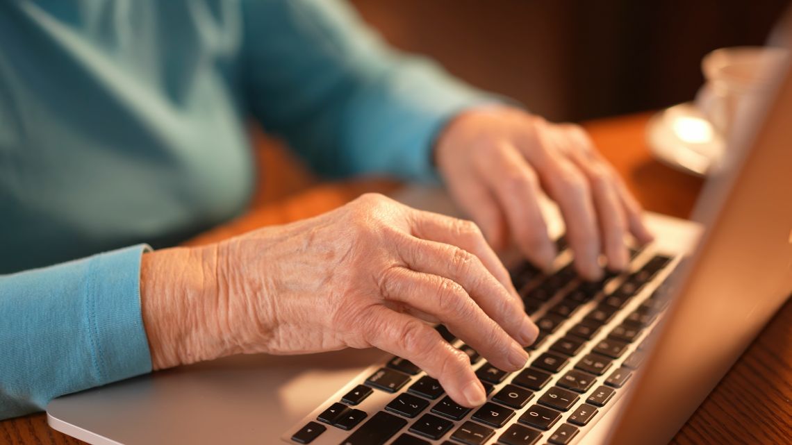 Hände einer Seniorin auf einer Laptoptastatur