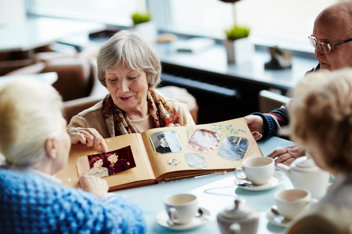 Seniorin zeigt am Kaffeetisch ihren Freundinnen Fotos im Fotoalbum