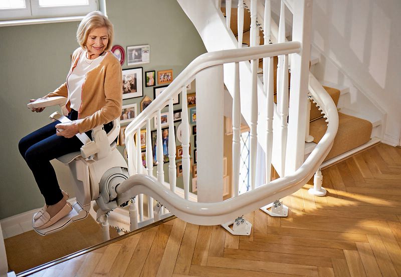 Eine Seniorin fährt auf einem Sitzlift die Treppe hinauf