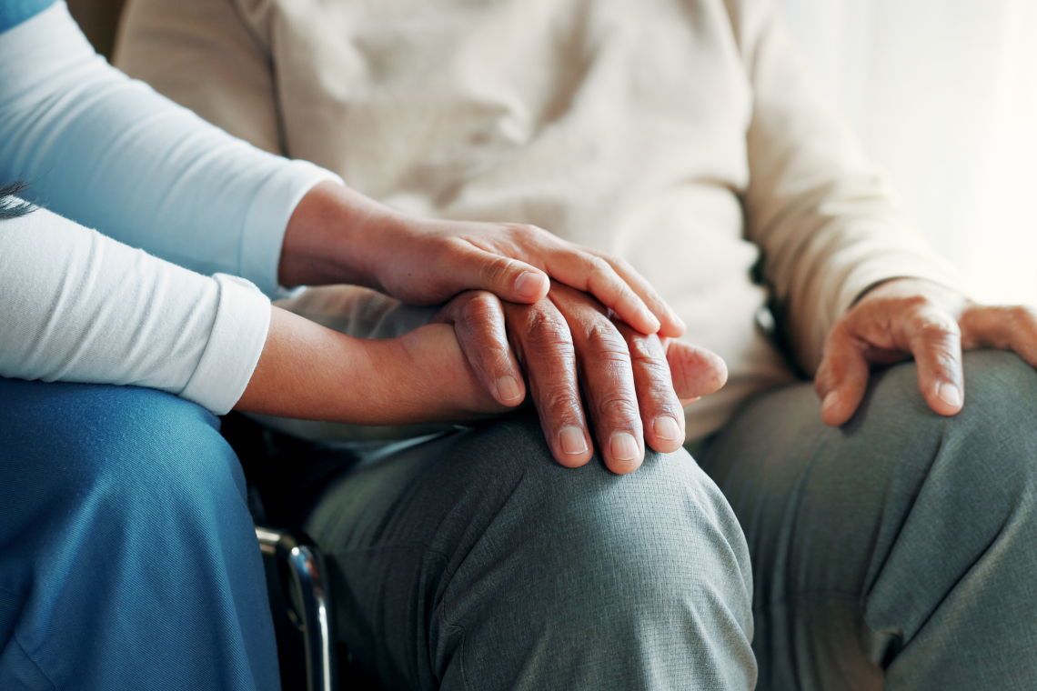 Eine Pflegekraft hält beruhigend die Hand einer älteren Person.
