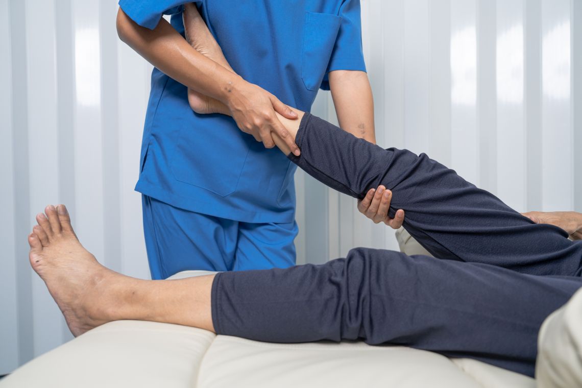 Eine Physiotherapeutin behandelt einen Mann mit schmerzenden Beinen