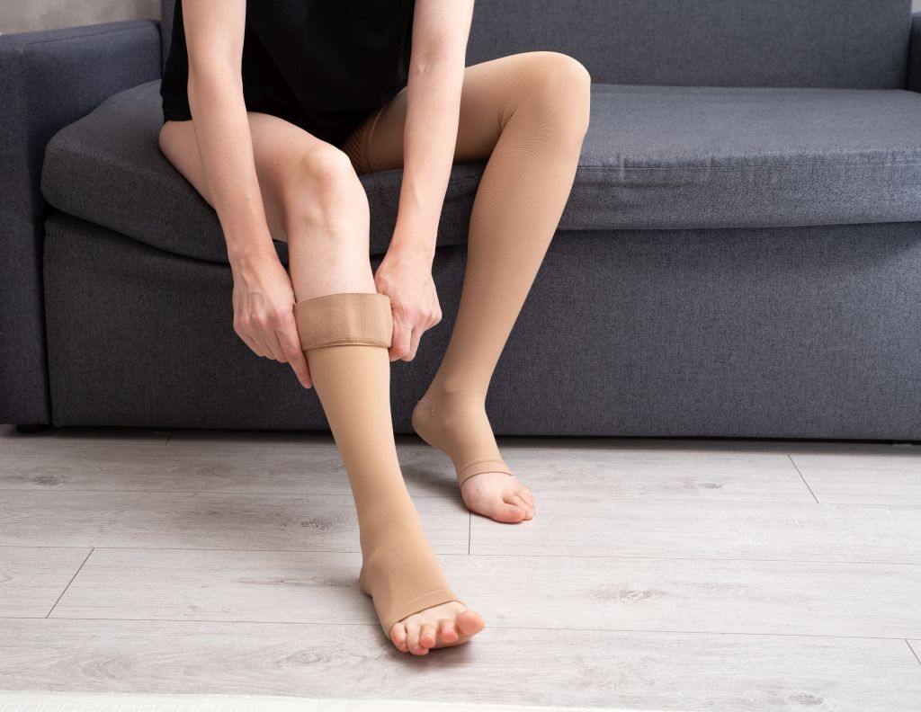 Eine Frau sitzt auf der Couch und zieht sich Kompressionstrümpfe an