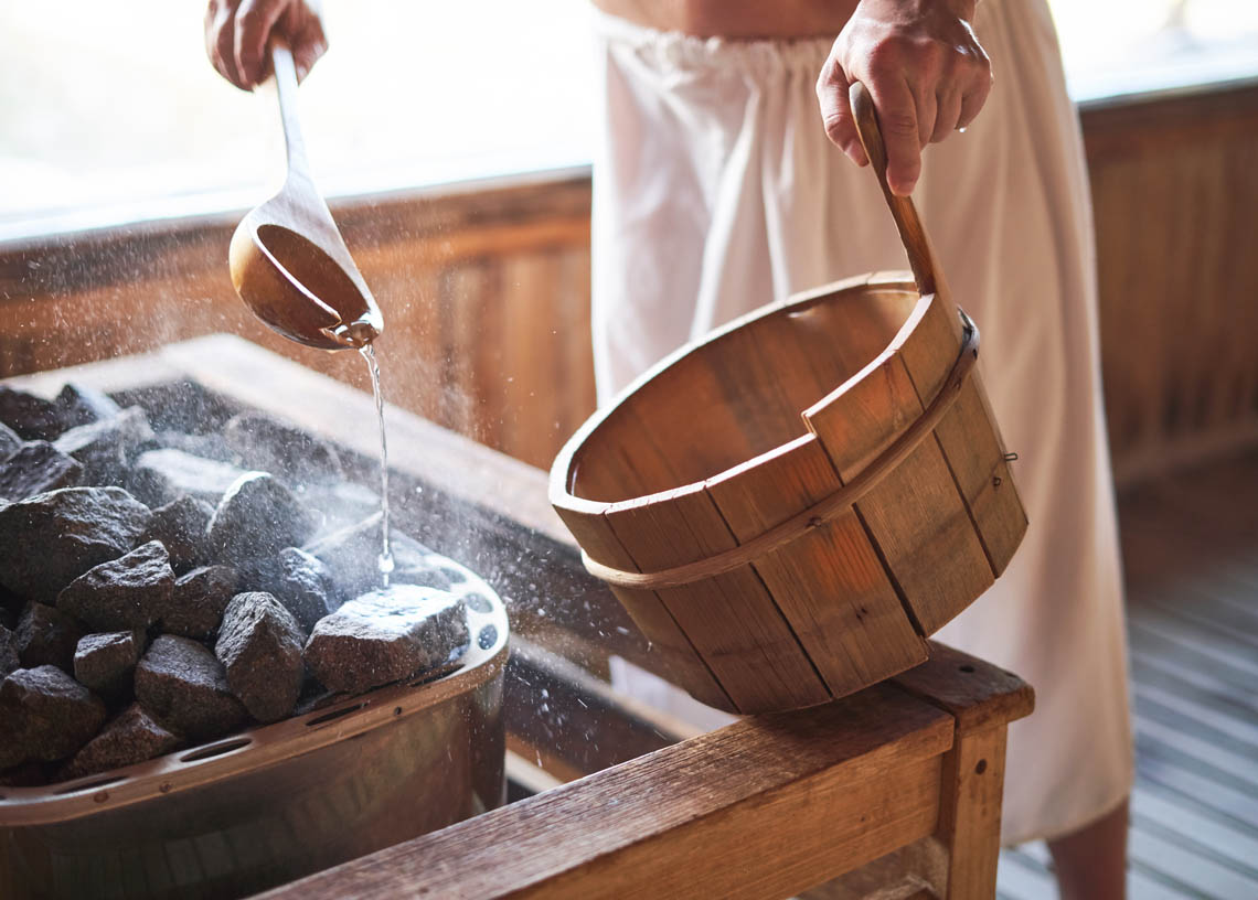 Senior gießt in Sauna Wasser auf heißen Stein