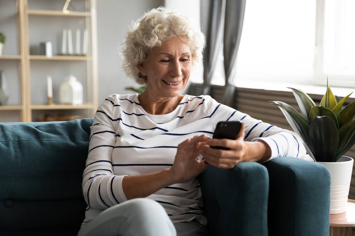 Frau sitzt auf dem Sofa und bedient ihr Seniorenhandy