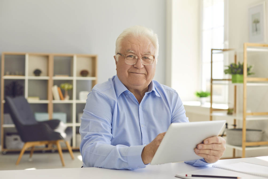 Senior sitzt zu Hause mit seinem Tablet