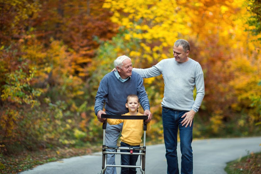 Testament aufsetzen: Rentner mit Rollator macht Spaziergang mit Enkelkind und Sohn