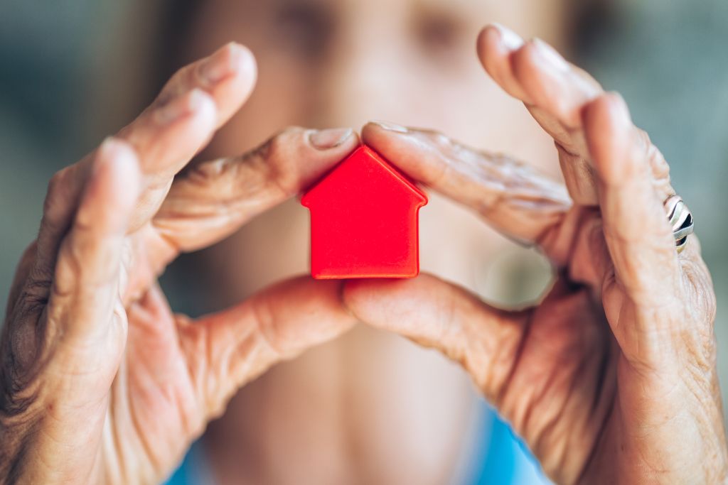 Testament aufsetzen: Frau hält kleines rotes Haus in Händen