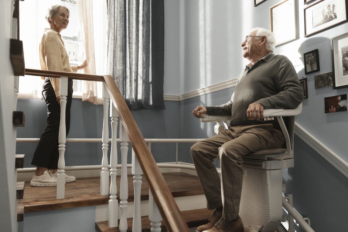 Ein älterer Mann fährt auf einem Sitzlift die Treppe hoch.