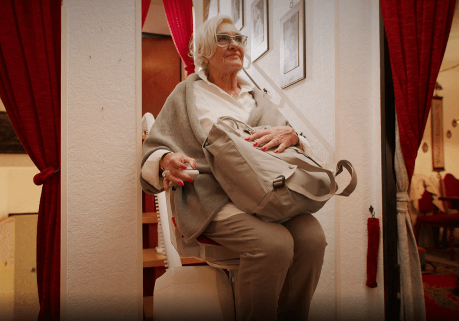 Ältere Frau sitzt auf Treppenlift mit Tasche auf dem Schoß