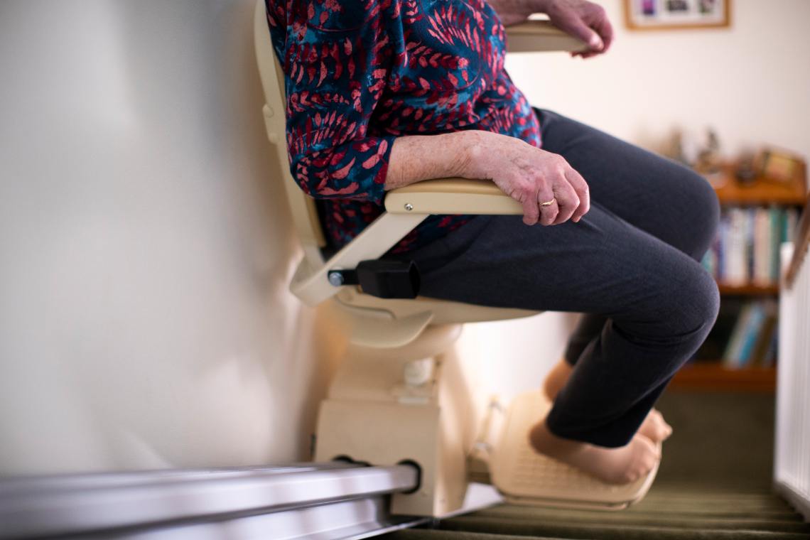 Günstige Treppenlifte kaufen © © Daisy Daisy | stock.adobe.com Frau fährt mit Sitzlift Treppen hinunter