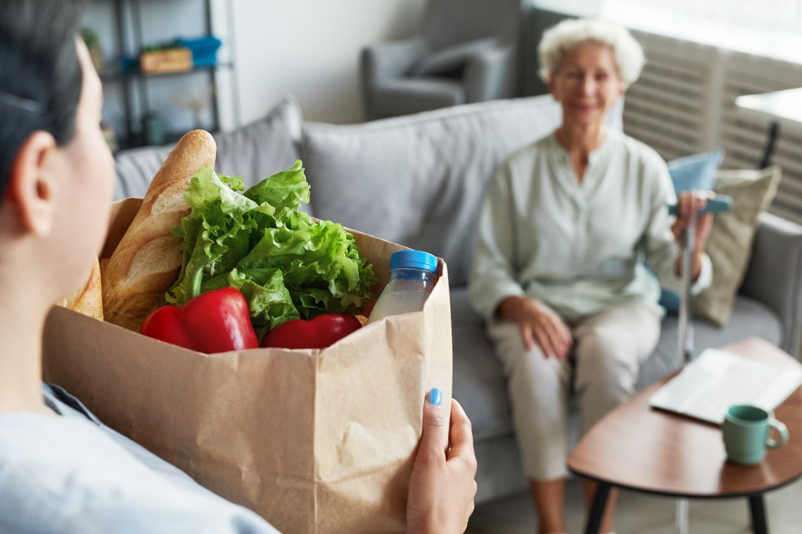 Einkaufen und andere Haushaltstätigkeiten können direkt nach der Operation überfordern. Pflegekraft bringt einer Seniorin den Lebensmitteleinkauf
