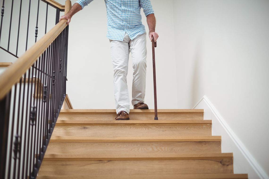 Nach einer Knie-Operation empfinden viele Menschen das Treppensteigen als besondere Hürde Senior läuft mit Gehstock eine Treppe runter