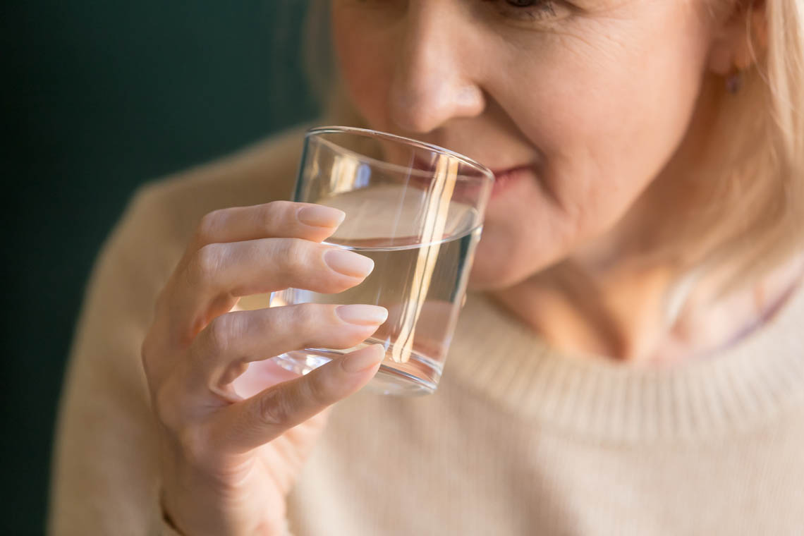 Seniorin trinkt stilles Wasser aus Glas