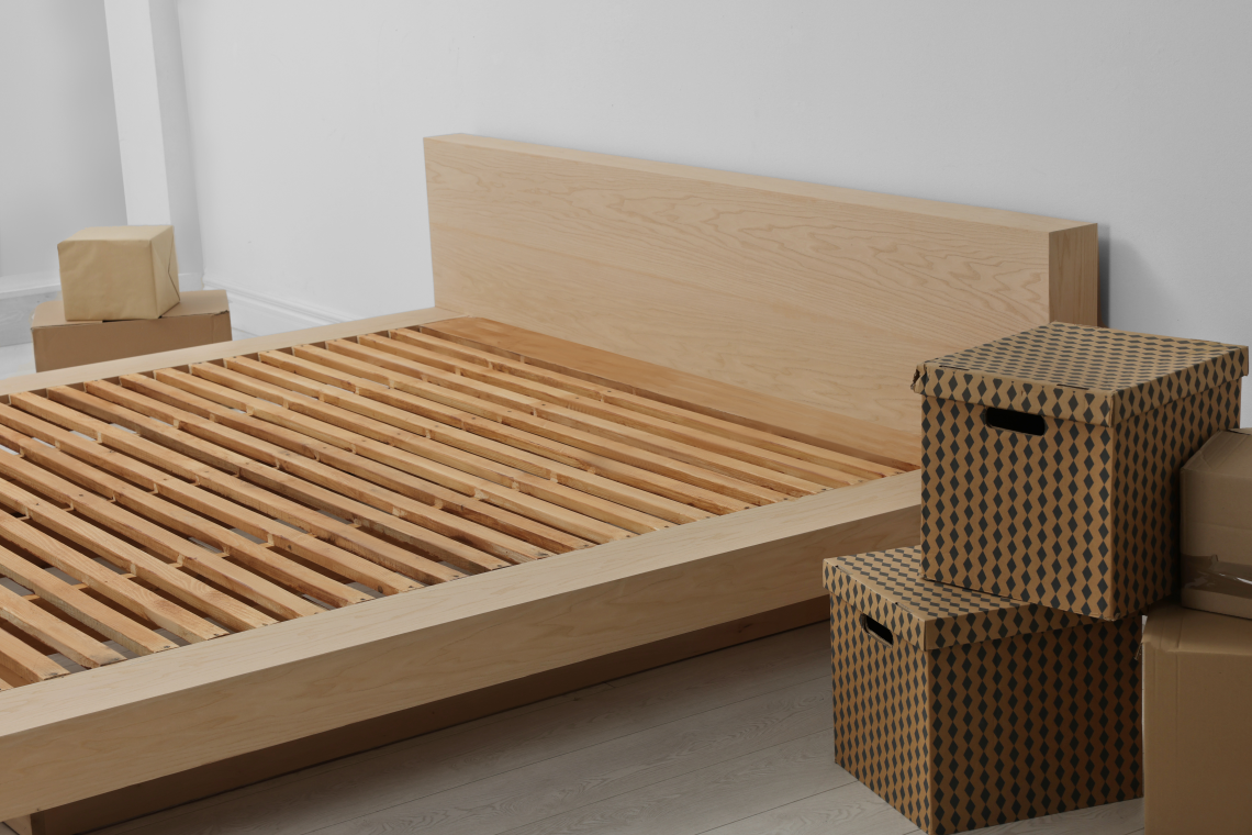 Bett ohne Matratze und Umzugskartons in einem Schlazimmer