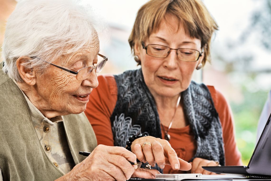 Eine Seniorin mit geistiger Einschränkung wird von einer Angehörigen beim Umgang mit Technik unterstützt.